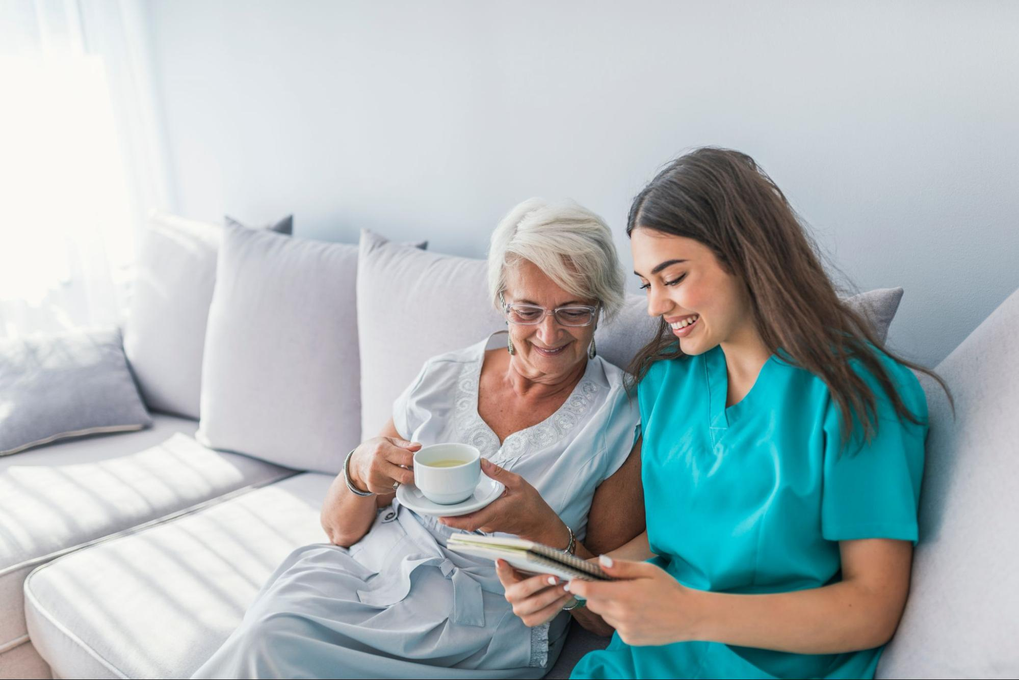 Caregiver sharing tea and conversation with an elderly woman on a sofa